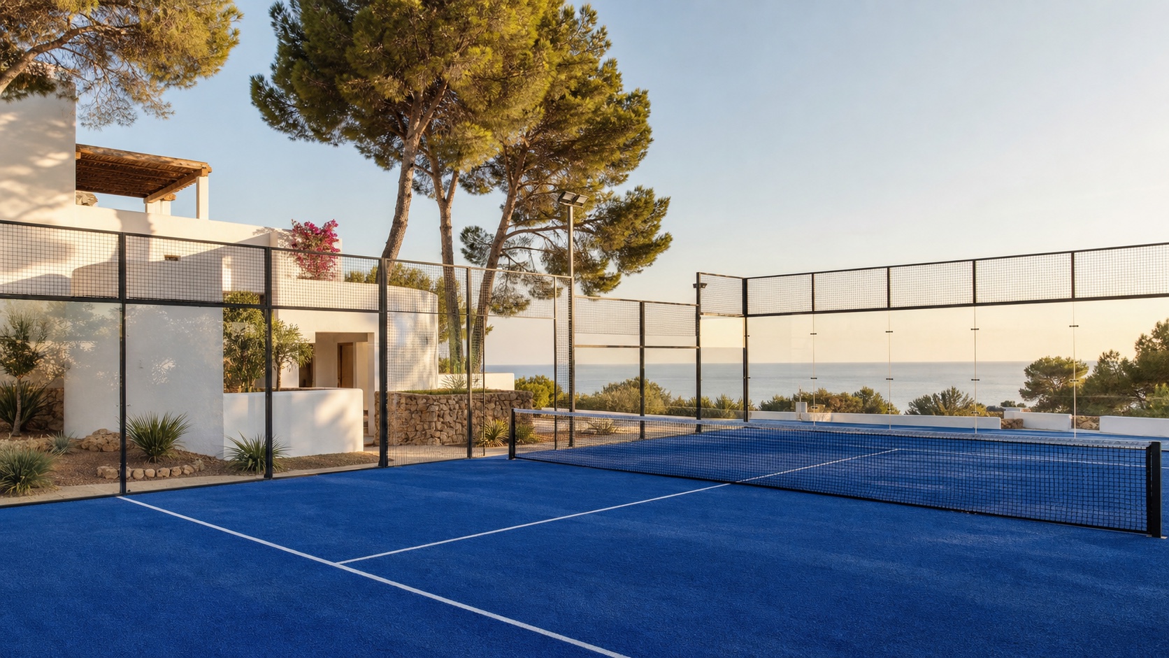 Eleganter blauer Padel-Court auf Ibiza zwischen weißen Häusern, Pinien und Mittelmeer